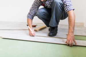 homem de camisa listrada colocando piso vinílico no chão de um cômodo