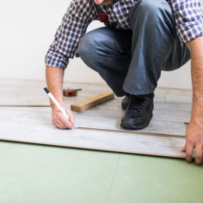 homem de camisa listrada colocando piso vinílico no chão de um cômodo