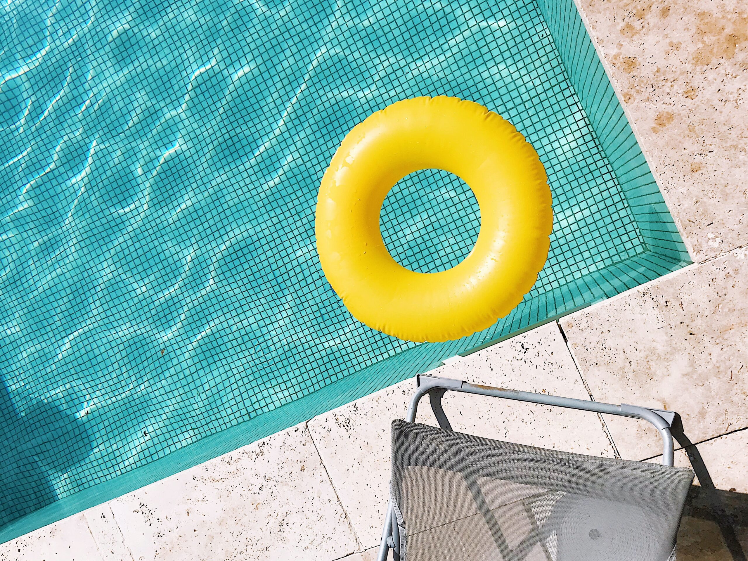 Piscina com revestimento claro, na superfície uma boia redonda amarela com furo no meio