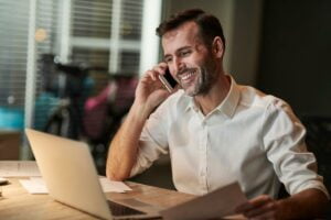 síndico sorrindo e olhando para o notebook enquanto conversa no celular