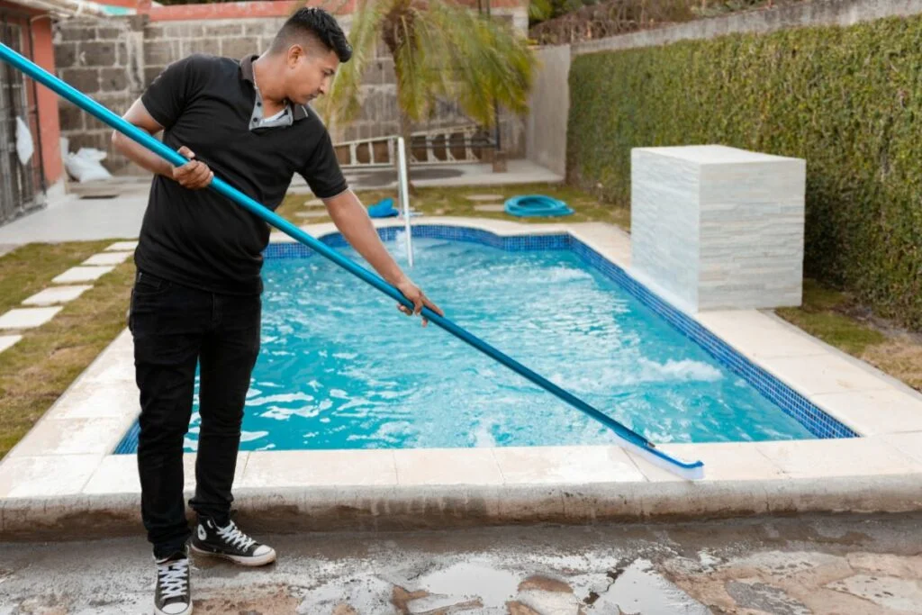homem varrendo no entorno da piscina